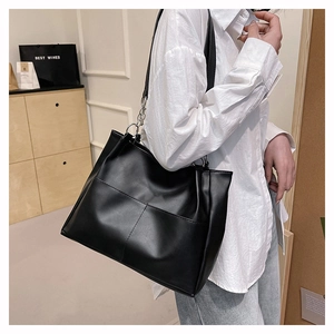 Detail of black leather tote bag featuring cross stitching and silver metal ring hardware