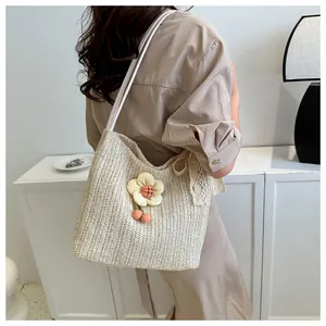 Detail of cream straw tote bag featuring yellow flower and red cherry pompom accent