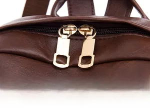 Detail of smooth golden metal double zippers on a dark brown leather backpack