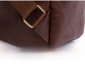 Detail view of reinforced triangular stitching and gold metal buckle on brown leather backpack