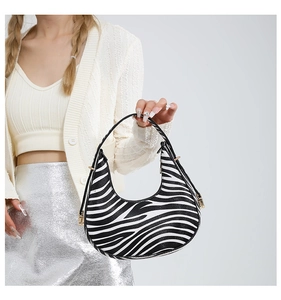 Detail of zebra pattern crescent bag with gold zipper on a fashion model in white