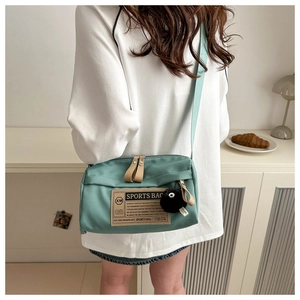 Detail van mintgroene Oxford crossbodytas met sportlogo en zwarte pluche hanger