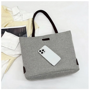 Detailed view of grey linen tote bag with brown straps and fashion label on white background