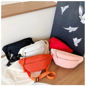 Five nylon crossbody waist bags in black, white, red, orange and pink on a wooden desk