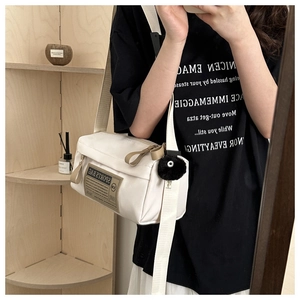 Detail van een witte Oxford crossbodytas met sportlabel en zwarte pompom-accessoire