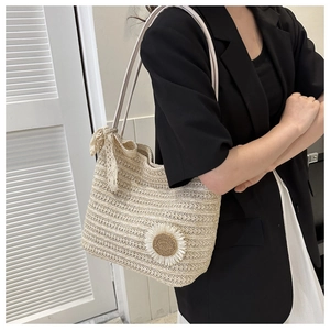 Detail of a straw tote bag with daisy ornament and lace ribbon on a model's shoulder