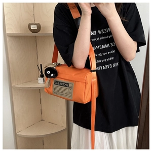 Detail van oranje nylon crossbodytas met geweven label en een zwart pluchen hangertje
