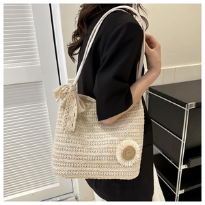 Detail of straw tote bag featuring lace bow and sunflower appliqué on beige woven texture