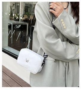 Close-up of a white nylon crossbody bag with silver butterfly and wide logo strap
