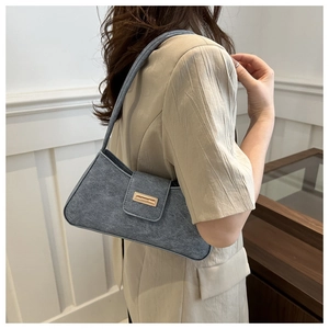 Detail view of a gray felt baguette shoulder bag on a beige blazer with a gold buckle