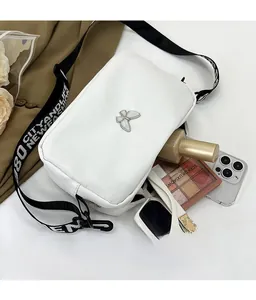 Detailed view of white crossbody bag with silver butterfly and wide jacquard strap