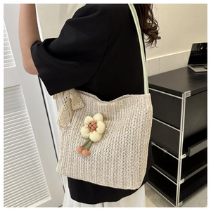 Detail of straw tote bag with knit flower charms and lace bow on green shoulder strap