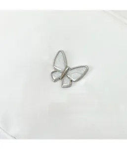 Detail of silver butterfly ornament with white enamel on a white woven fabric bag