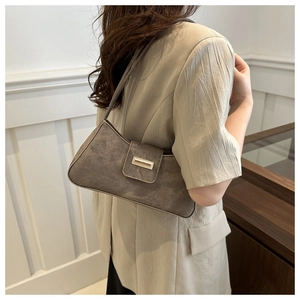 Detailed view of a coffee brown suede baguette bag with an elegant gold buckle on a model