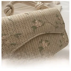 Detail of woven straw handbag featuring delicate floral embroidery and knotted rope handles