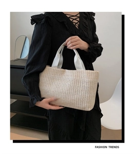 Détail d'un sac cabas en paille tissée avec anses en toile blanche sur une robe noire élégante