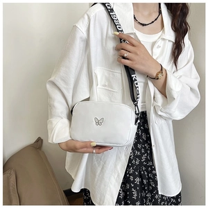 Close-up of white nylon crossbody bag featuring silver butterfly logo and lettered strap