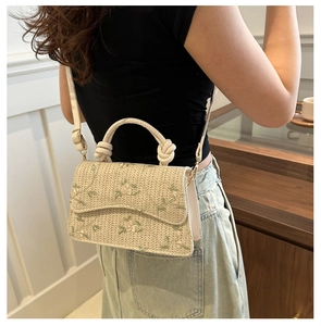 Close-up of straw crossbody bag with floral embroidery worn by a model in a casual setting