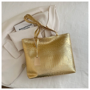 Detailaufnahme einer goldenen Einkaufstasche mit Krokodil-Prägung und Metallanhänger