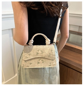 Detail of woven straw handbag with floral embroidery and knotted handle on model