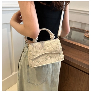 Detail of woven straw crossbody bag with floral embroidery and unique knotted handle