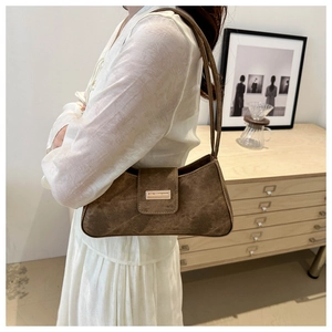 Detail of a brown suede baguette bag with a minimalist metal buckle on a shoulder strap