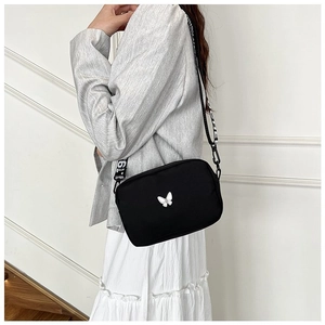 Detail of black nylon crossbody bag with white butterfly and logo strap on model