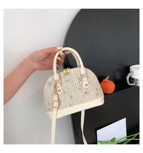 Detail of hand-woven straw shell bag with delicate floral embroidery and gold dual zippers