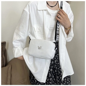 Detail of white nylon crossbody bag featuring silver butterfly badge and wide logo strap