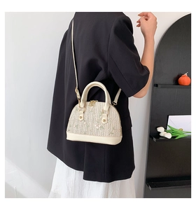 Detail of beige straw shell bag with green floral embroidery worn with a black blazer