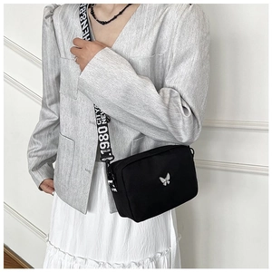 Detail of minimalist nylon crossbody bag featuring silver butterfly logo and wide logo strap