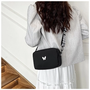 Detail of nylon crossbody bag featuring a white butterfly motif and lettered strap