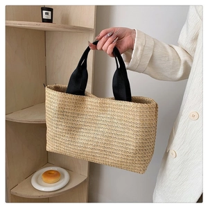 Gros plan détaillé d'un sac cabas en paille beige avec anses tissées noires et grand espace