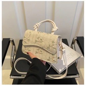 Close-up of woven straw handbag with floral embroidery and braided knot handle