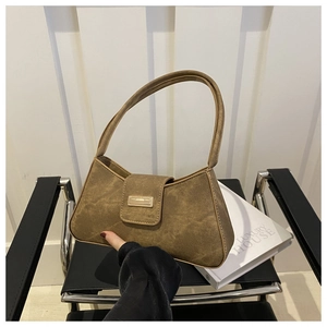 Detail of a brown suede baguette bag with a gold metal buckle on a black chair