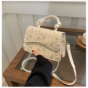 Detail of woven straw bag featuring floral embroidery and knotted handle detail