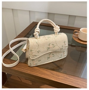 Detail of hand-woven straw crossbody bag featuring green leaf and pink floral embroidery