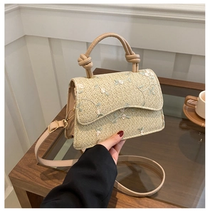 Detail of woven straw bag featuring floral embroidery and knotted rope handles for summer