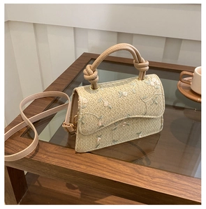 Detail of floral embroidery on beige woven straw handbag with knotted round handle