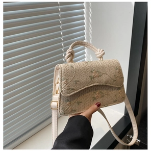 Close-up of white woven straw crossbody bag with floral embroidery and twisted handle