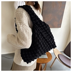 Détail du grand sac cabas noir à texture gaufrée porté à l'épaule par un mannequin chic