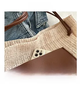 Detail view of woven straw tote bag featuring a brown leather pocket and smartphone inside