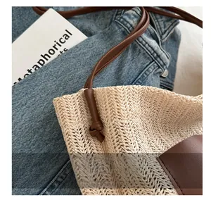Detail of woven straw tote bag with brown leather straps on a denim background