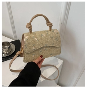 Detail of woven straw handbag with floral embroidery and knotted top handle strap