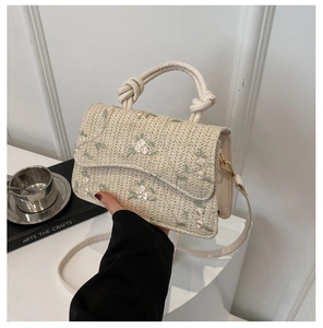 Detail of woven straw handbag featuring white floral embroidery and twisted rope handle