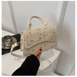 Detail of woven straw bag with floral embroidery, knot handle and golden hardware