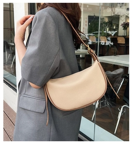 Chic beige half-moon shoulder bag in pebble leather worn by a model in a modern grey suit