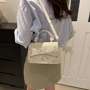 Elegant woven straw crossbody bag with floral embroidery and twisted handle shown on model
