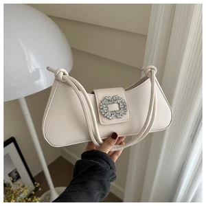 Close-up of cream underarm bag with a sparkling rhinestone buckle and knotted straps