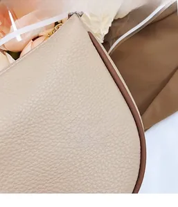 Detailed close-up showing the litchi grain texture and gold zipper of the beige crossbody bag